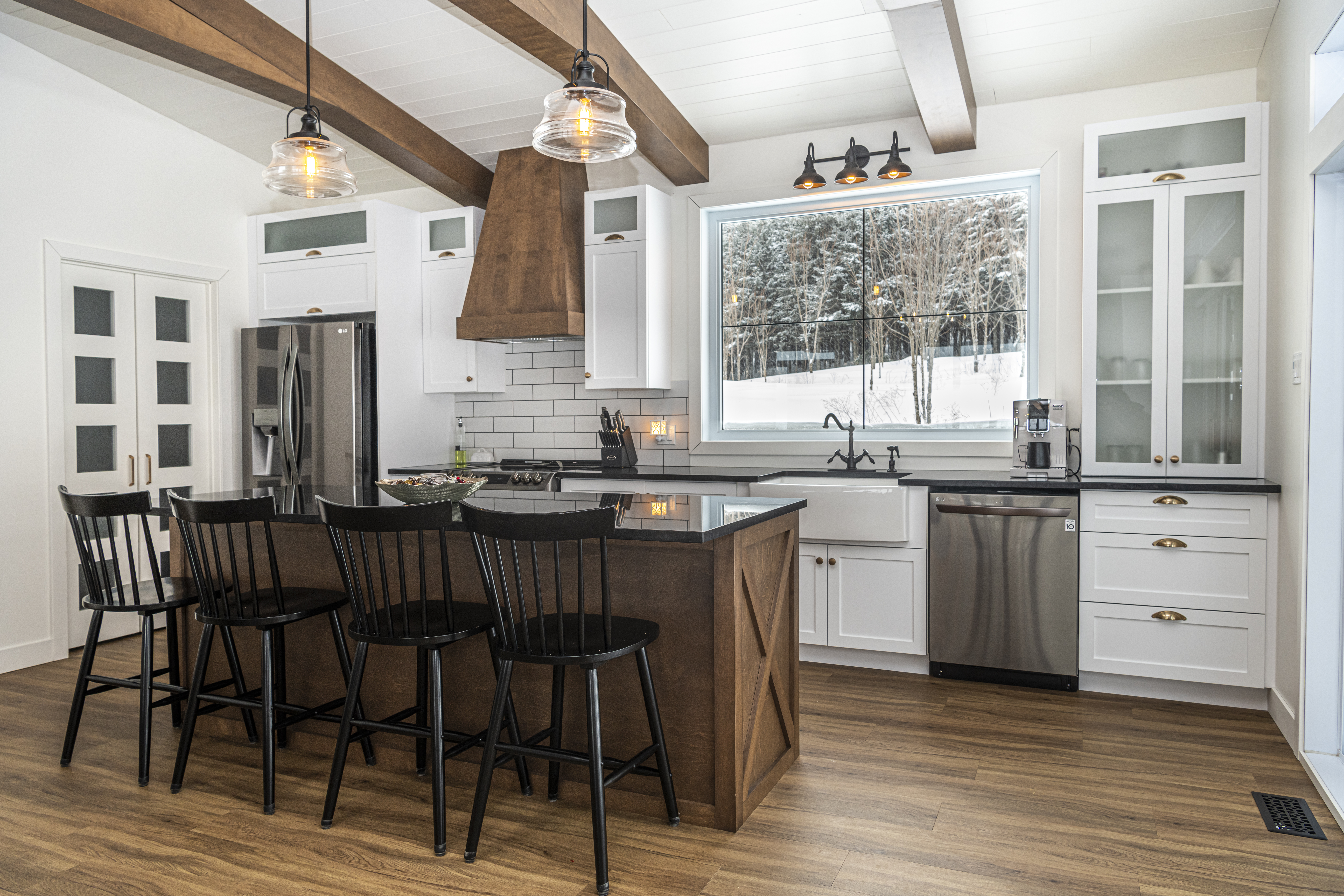 Mélange de blanc, noir et bois. Cuisine avec évier à tablier et cache hotte en bois. Comptoir de granit Saint-Henry