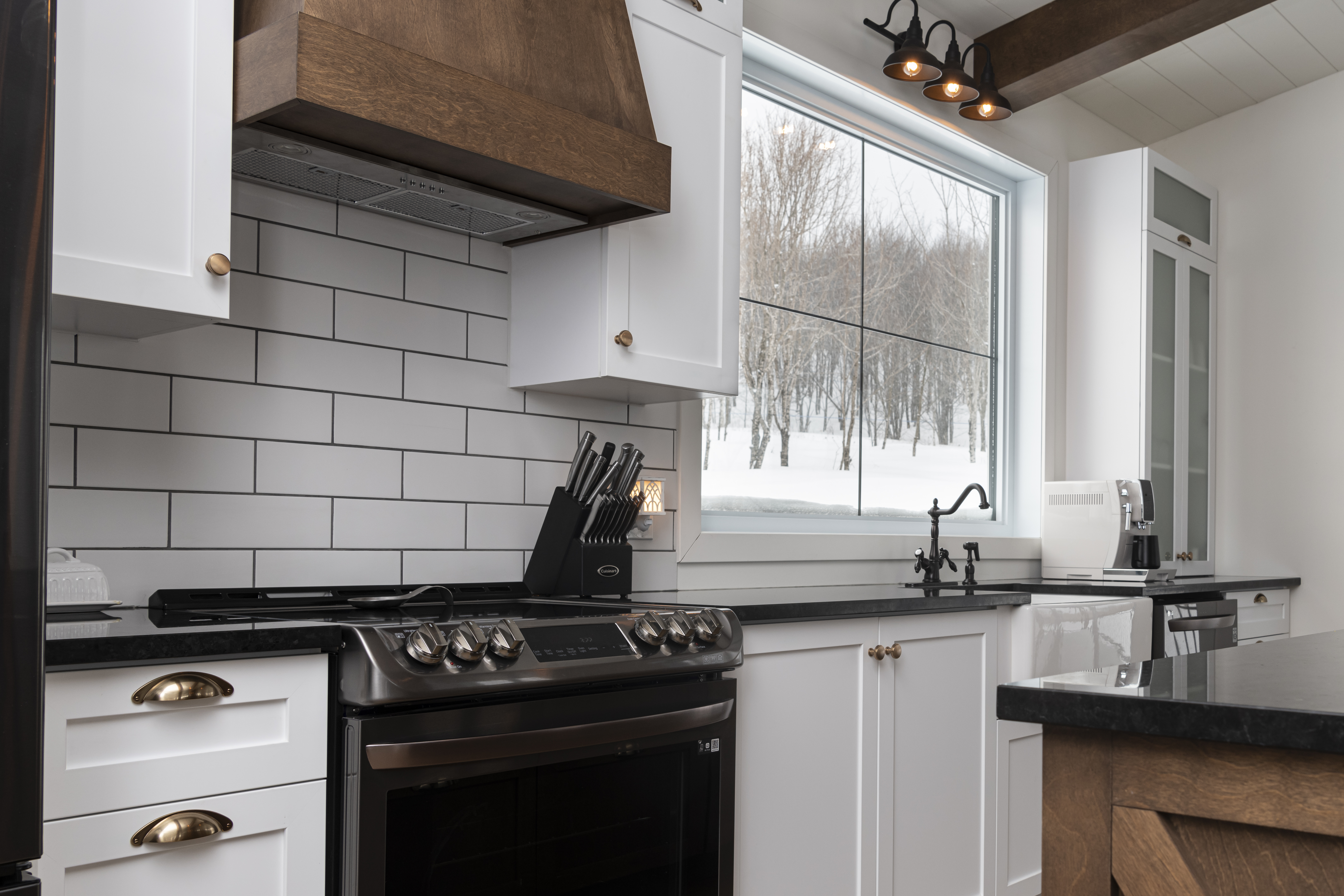 Mélange de blanc, noir et bois. Cuisine avec évier à tablier et cache hotte en bois. Comptoir de granit Saint-Henry