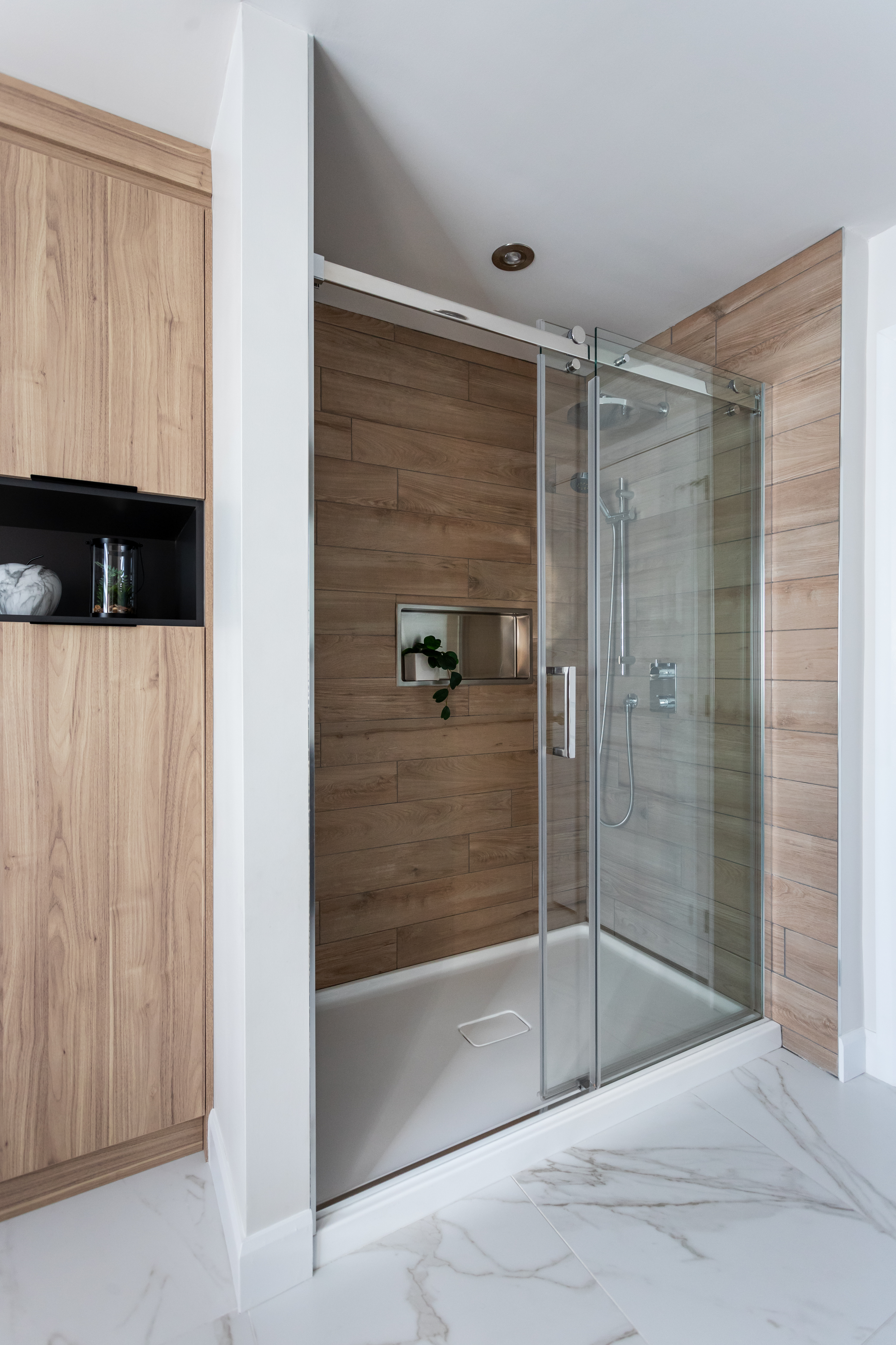 Grande douche en alcôve avec porcelaine effet bois et une niche pour toujours plus de rangement. 