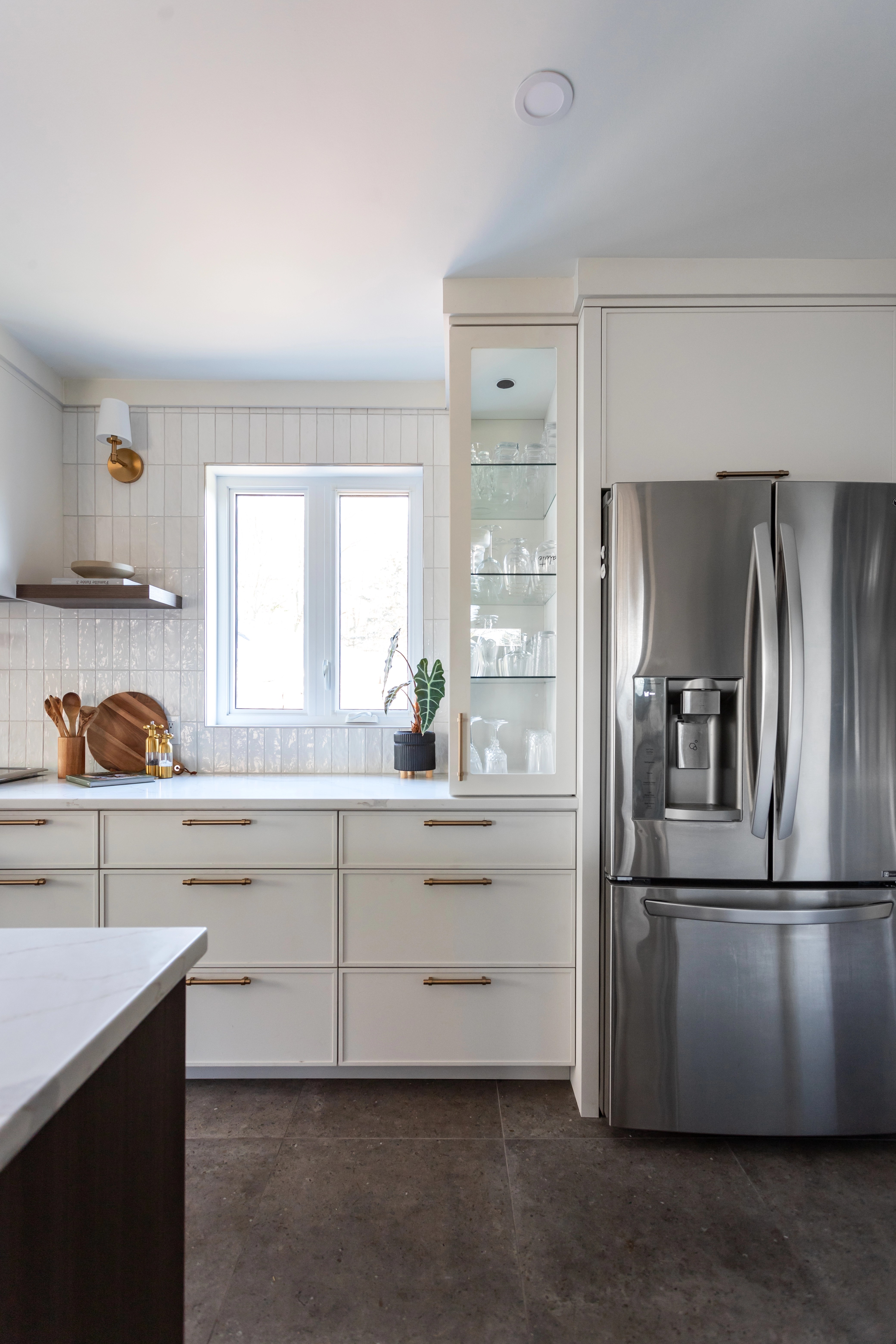 Cuisine lumineuse avec comptoir en quartz blanc et armoires sur mesure - porte shaker slim greige et accent d'effet bois. Rénovation rez-de-chaussée à Bécancour, Trois-Rivières. Réalisée par les designers d'intérieur de chez Élévation Studio Design.