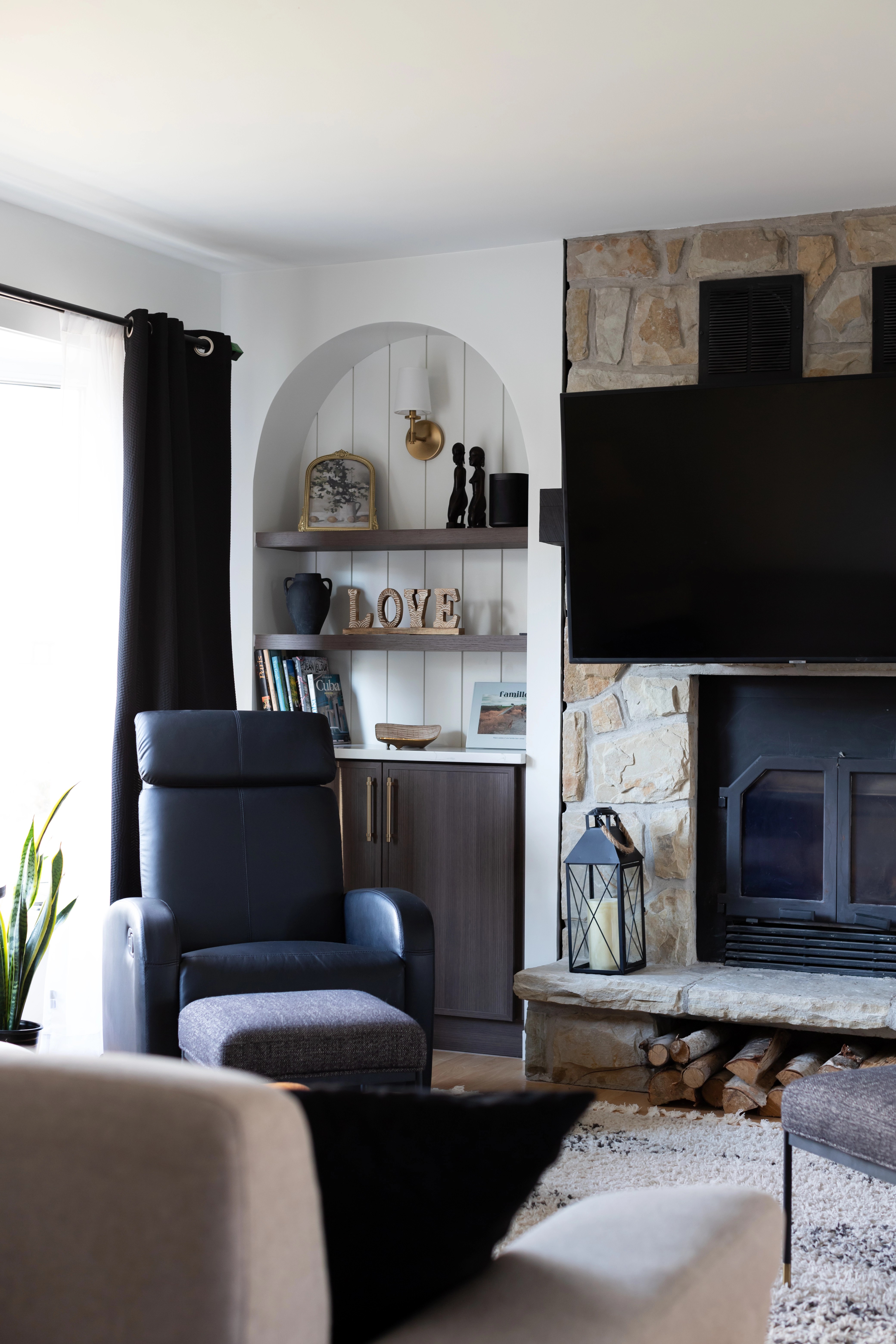 Salon chaleureux avec foyer en pierre, built-in en forme d'arche de chaque côté du foyer, rangement intégré de chaque côté du foyer en forme d'arche, tv au-dessus du foyer, poutres apparentes. Projet de design intérieur résidentiel à Bécancour, Trois-Rivières, Québec par Élévation Studio Design