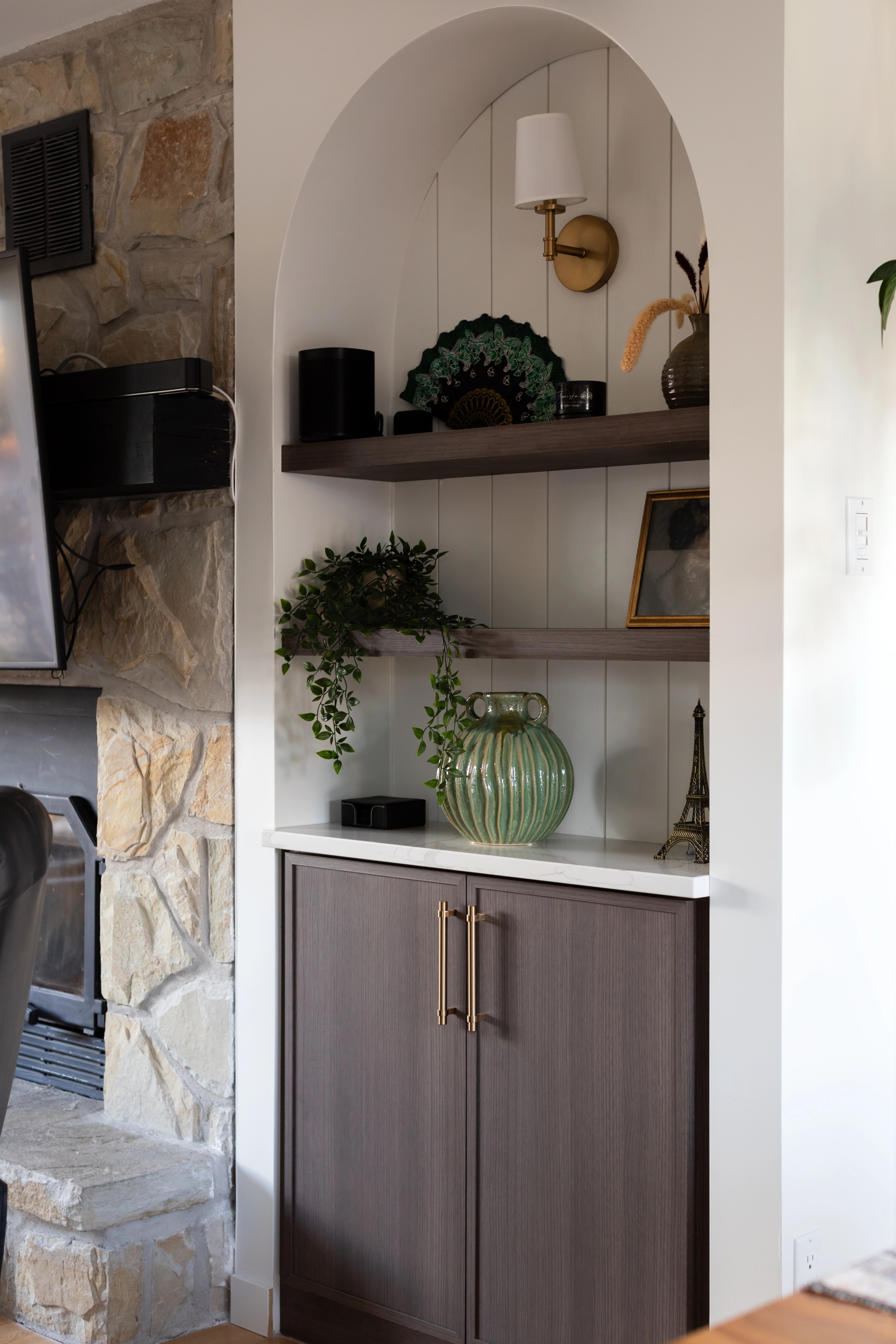 Salon chaleureux avec foyer en pierre, built-in en forme d'arche de chaque côté du foyer, rangement intégré de chaque côté du foyer en forme d'arche, tv au-dessus du foyer, poutres apparentes. Projet de design intérieur résidentiel à Bécancour, Trois-Rivières, Québec par Élévation Studio Design