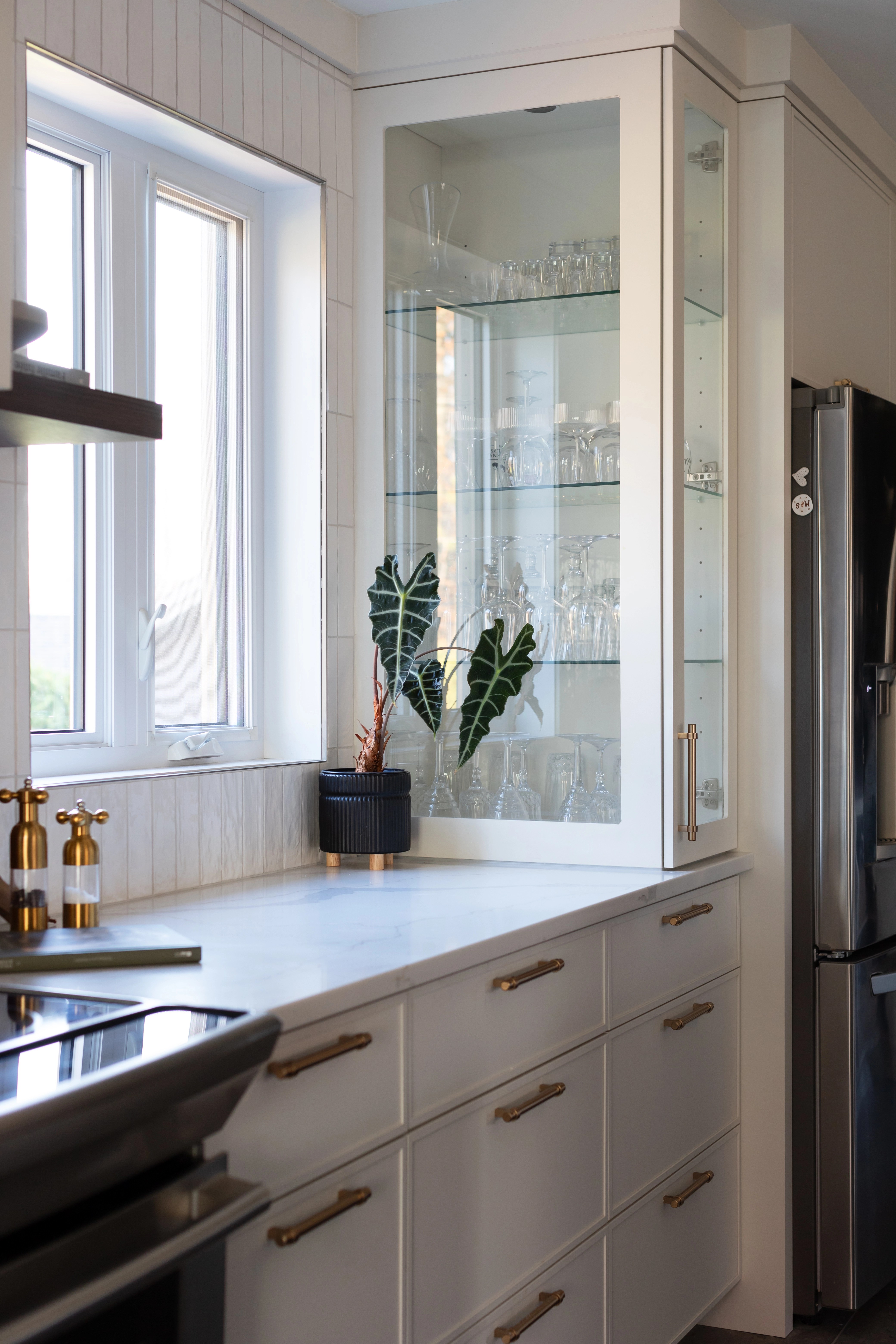 Cuisine lumineuse avec armoire vitré en coin sur le comptoir de la cuisine, armoire vitré pour les verres, armoire vitré sur mesure sur le comptoir. Design, cuisiniste, designer design d'intérieur réalisée par Élévation Studio Design.