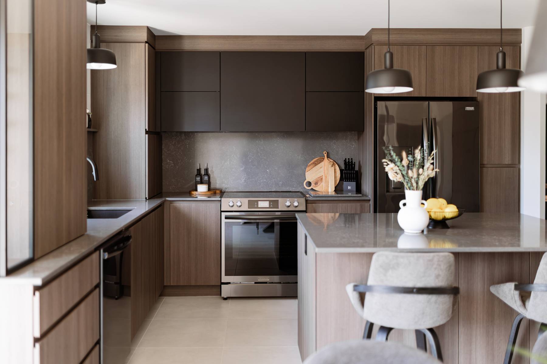 Rénovation de cuisine moderne en bois et noir mat avec îlot central et comptoir de quartz gris. Style chaleureux et contemporain à Acton Vale, Québec, signé Élévation Studio Design.