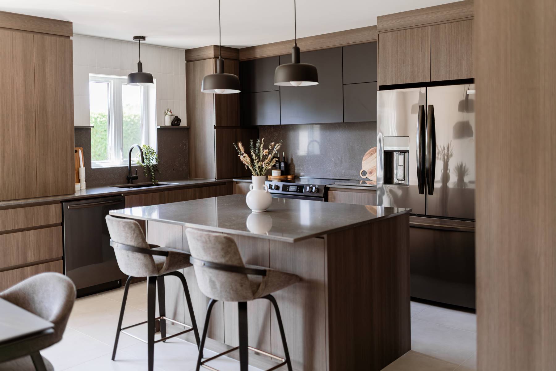 Cuisine sur mesure avec armoires de bois texturé et accents noirs, grand îlot convivial et rangement intégré. Design épuré et fonctionnel par Élévation Studio Design à Acton Vale.