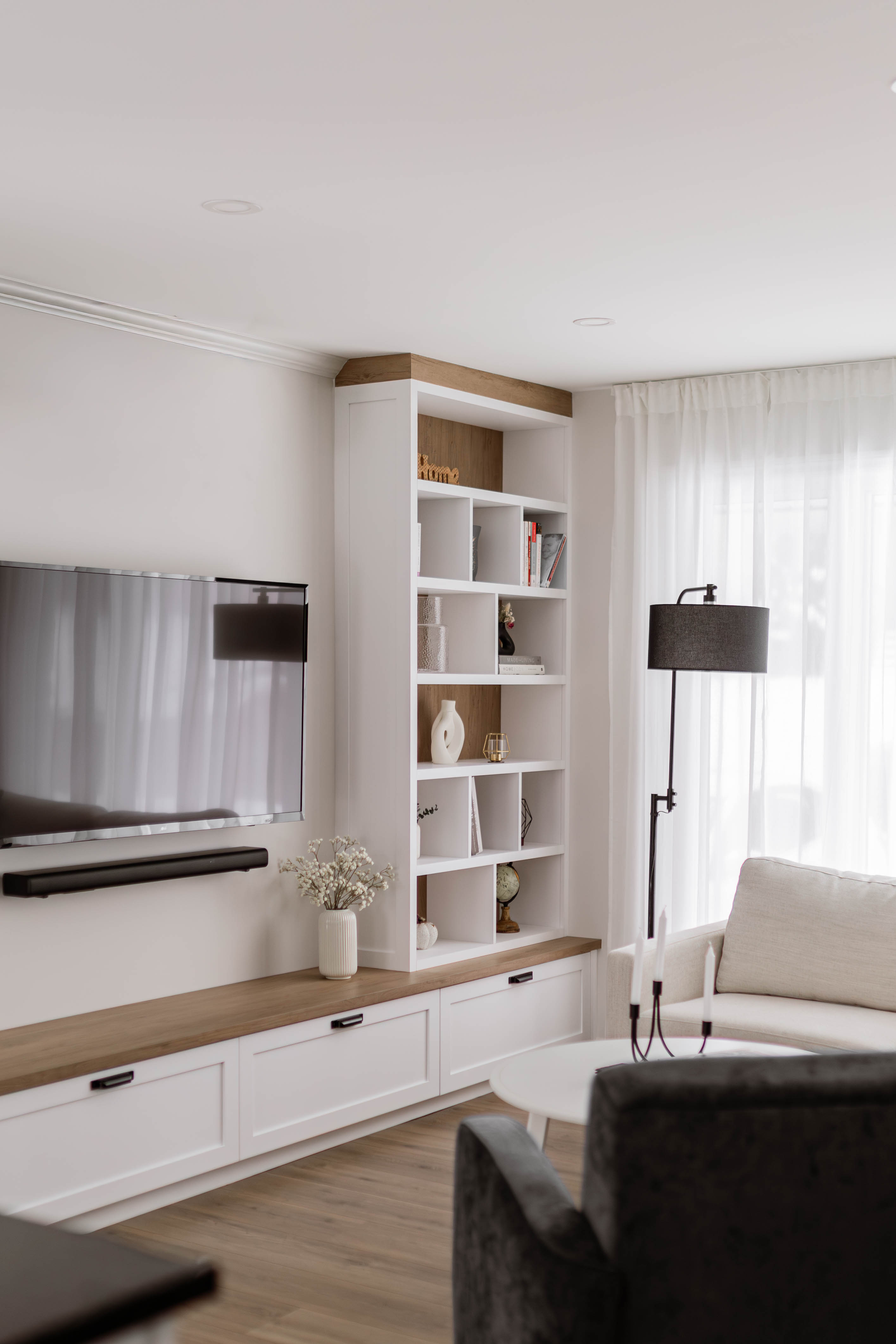 Meuble multimédia et bibliothèque sur mesure blanche avec une touche d'effet bois dans un salon moderne avec une touche de farmhouse - par les designer d'intérieur de chez Élévation Studio Design à Thetford Mines