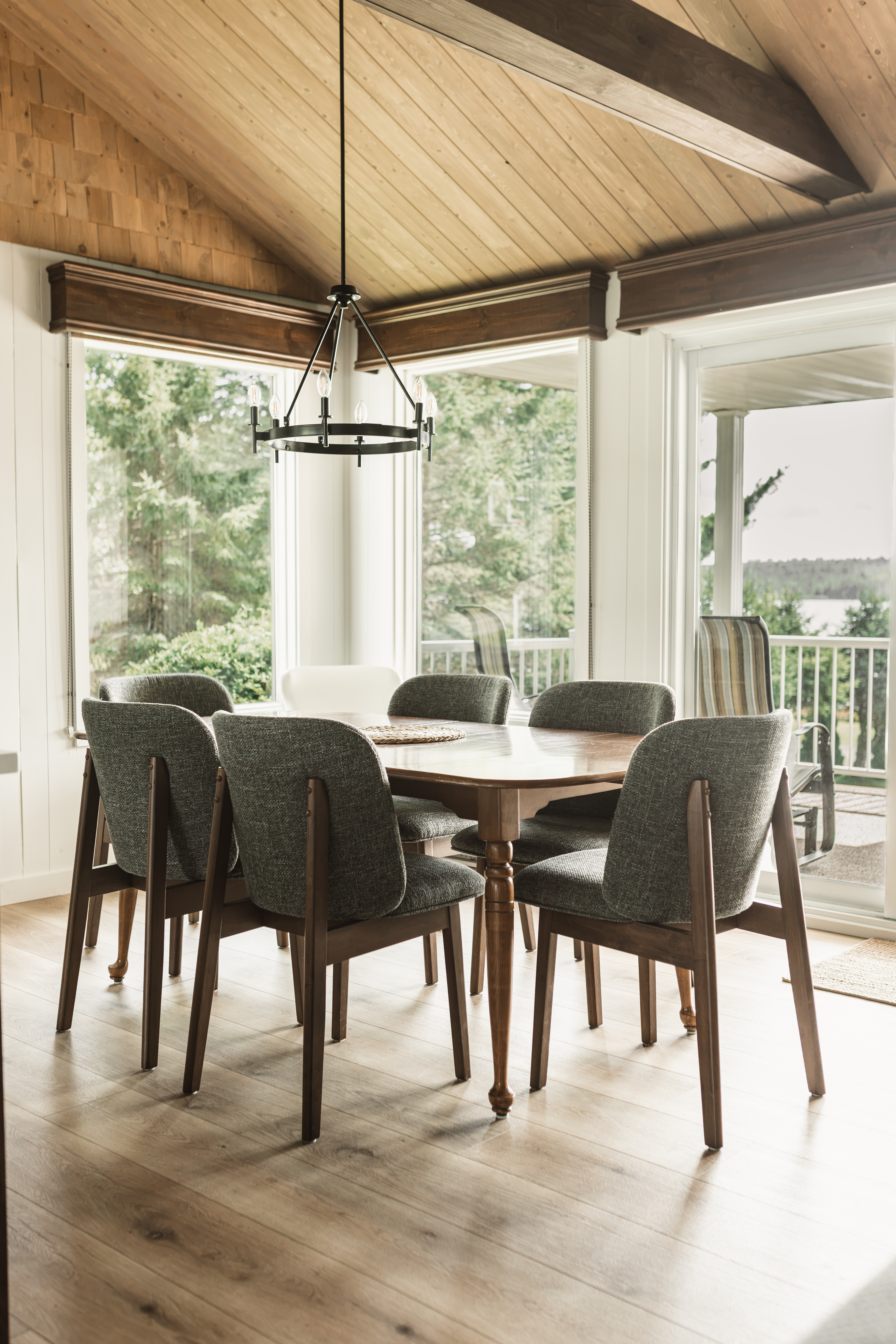 Salle à manger d'un chalet familial rénové de style farmhouse avec table en bois, chaises foncées et plafond cathédrale en bois
