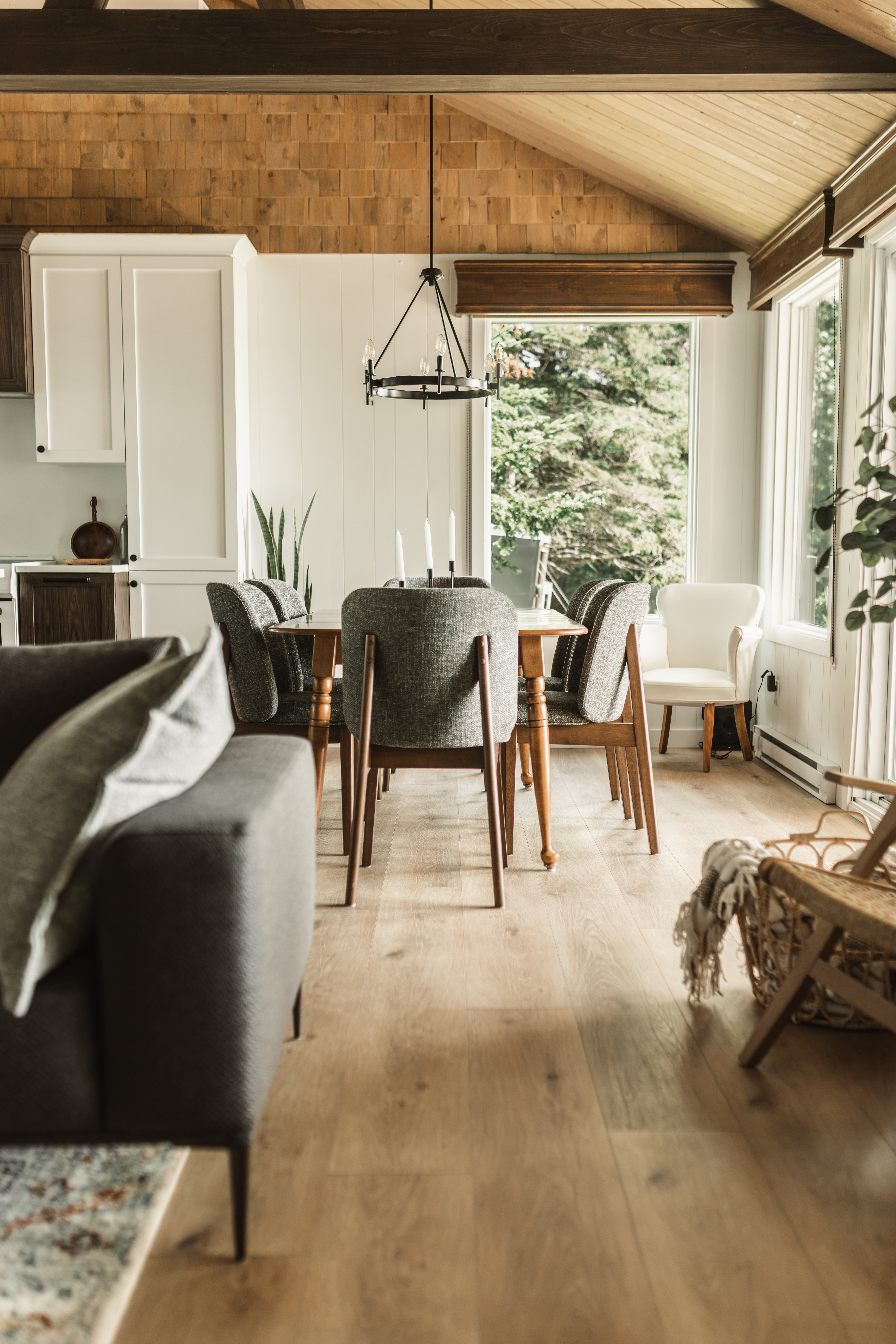 Aire ouverte d'un chalet rénové à Disraeli reliant la salle à manger, la cuisine et le salon, avec plancher effet bois clair et grandes fenêtres | rénovation de chalet avec mur retiré | designer d'intérieur, Élévation Studio Design à Thetford Mines