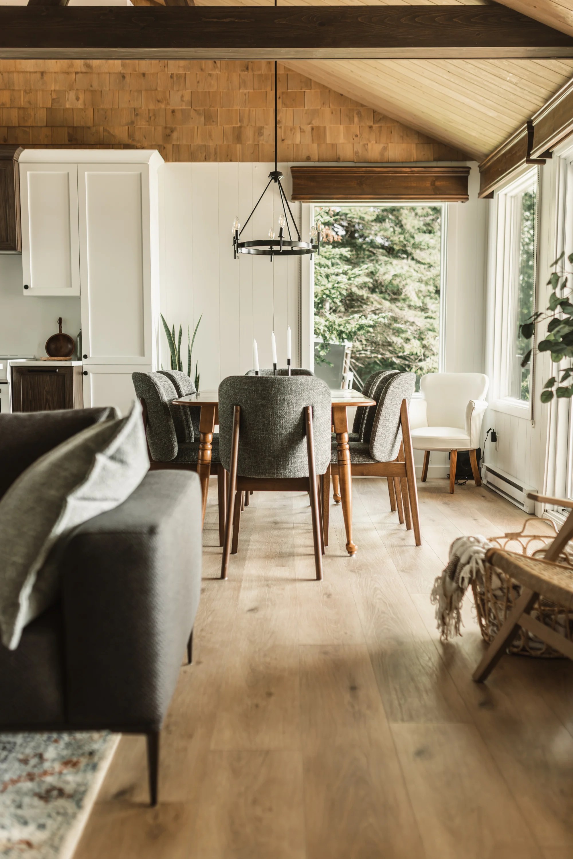 Aire ouverte d'un chalet rénové à Disraeli reliant la salle à manger, la cuisine et le salon, avec plancher effet bois clair et grandes fenêtres