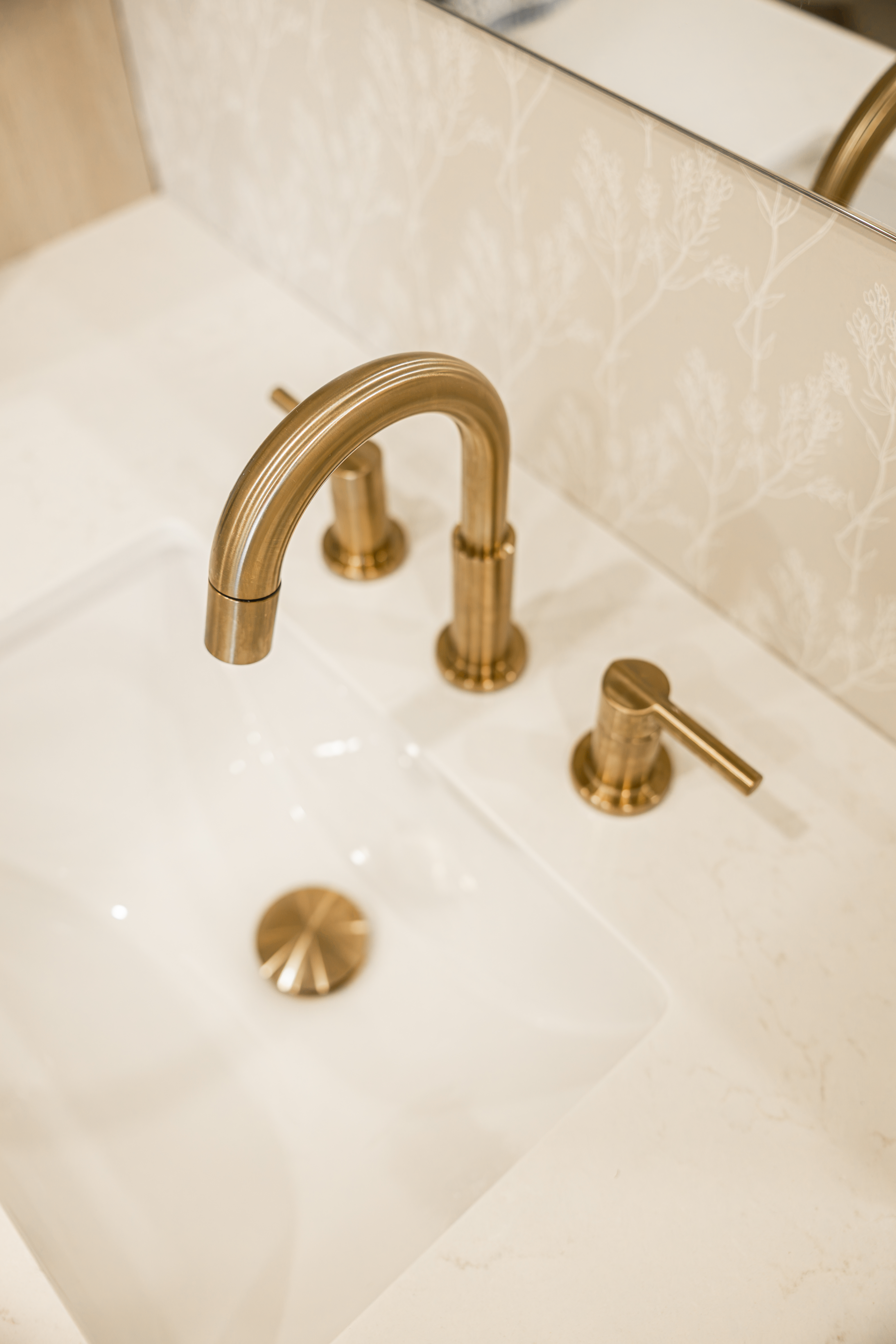 Détail d'un robinet doré et d'un lavabo sous comptoir (lavabo sous plan) en quartz blanc