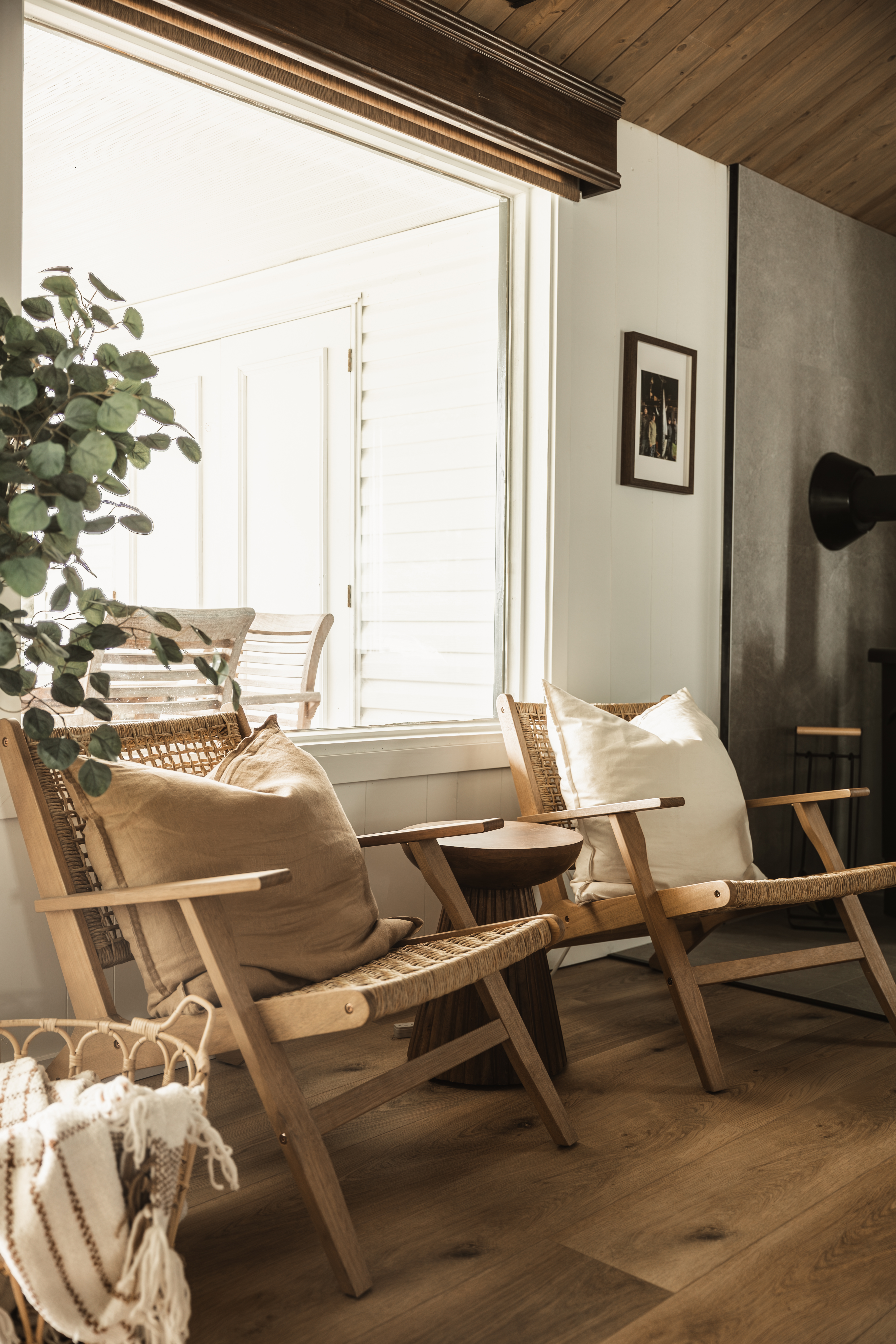 Coin salon avec fauteuils en bois et cannage, plantes et grandes fenêtres dans un chalet rénové à Thetford Mines