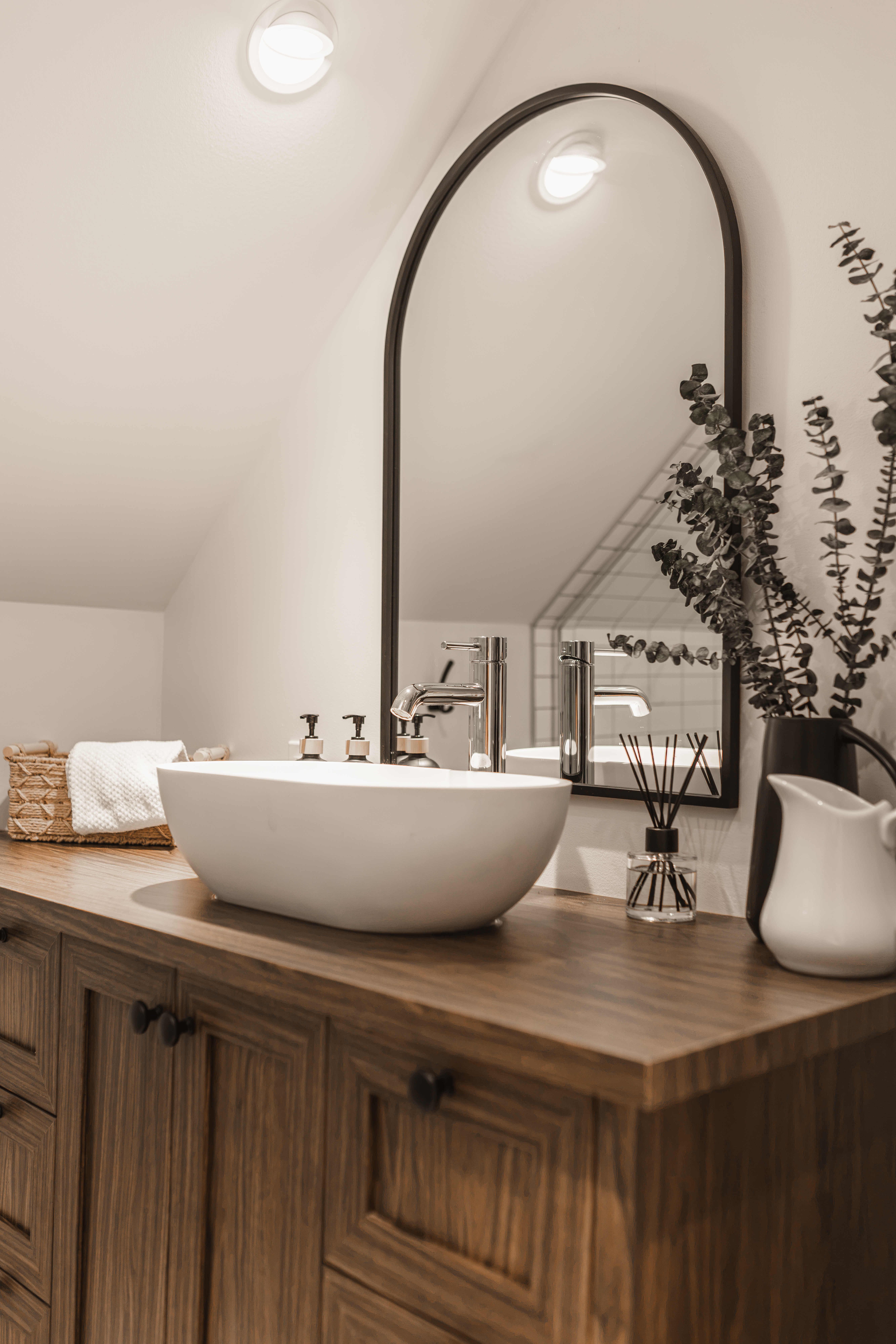 Salle de bain de la mezzanine avec vasque ronde, vanité en bois et miroir en arche sous un plafond mansardé | rénovation de salle de bain de chalet | designer d'intérieur, Élévation Studio Design à Thetford Mines