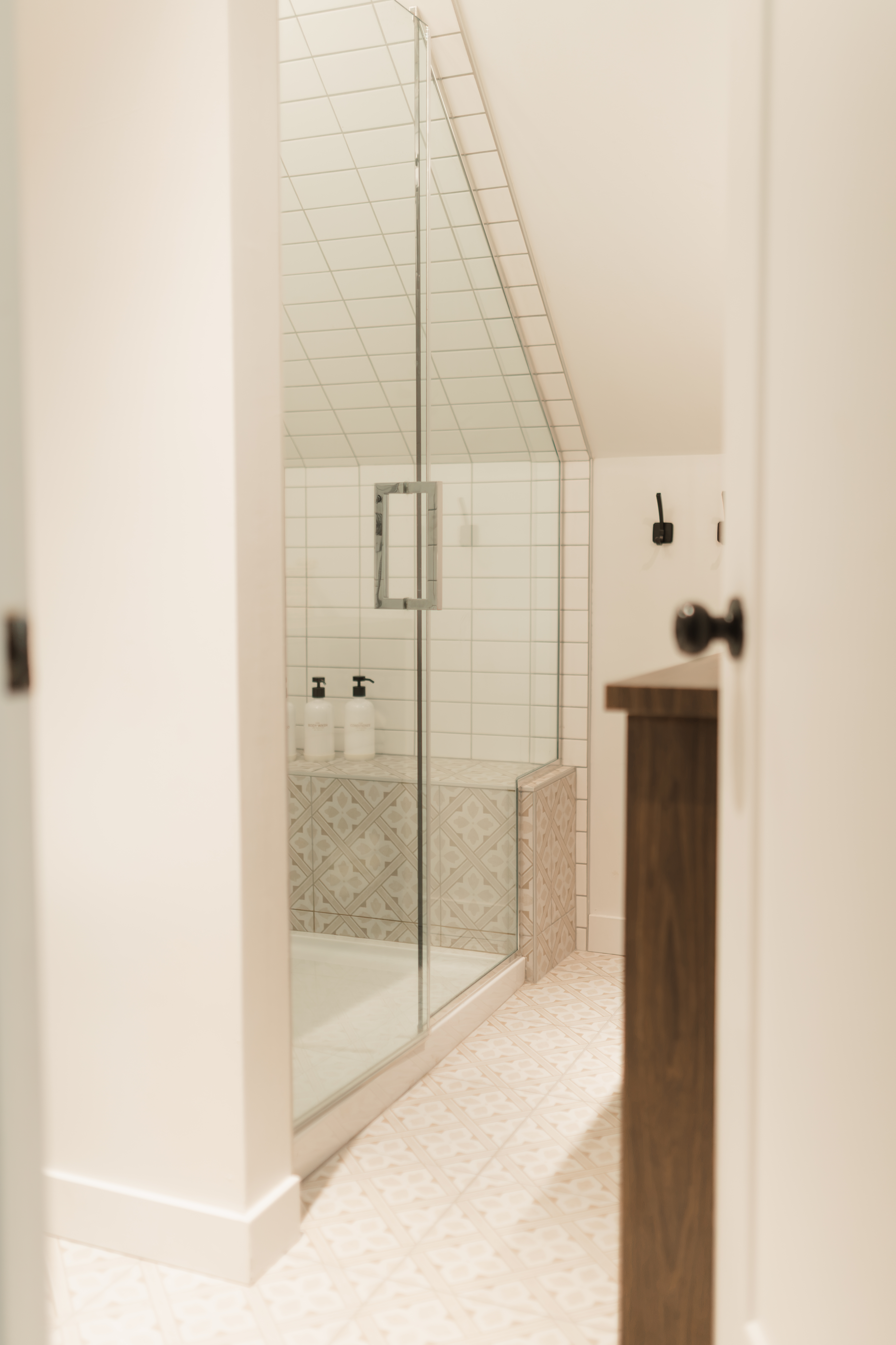 Douche vitrée avec carrelage blanc et plafond mansardé dans la salle de bain de la mezzanine du chalet que Élévation Studio Design a concu le design complet