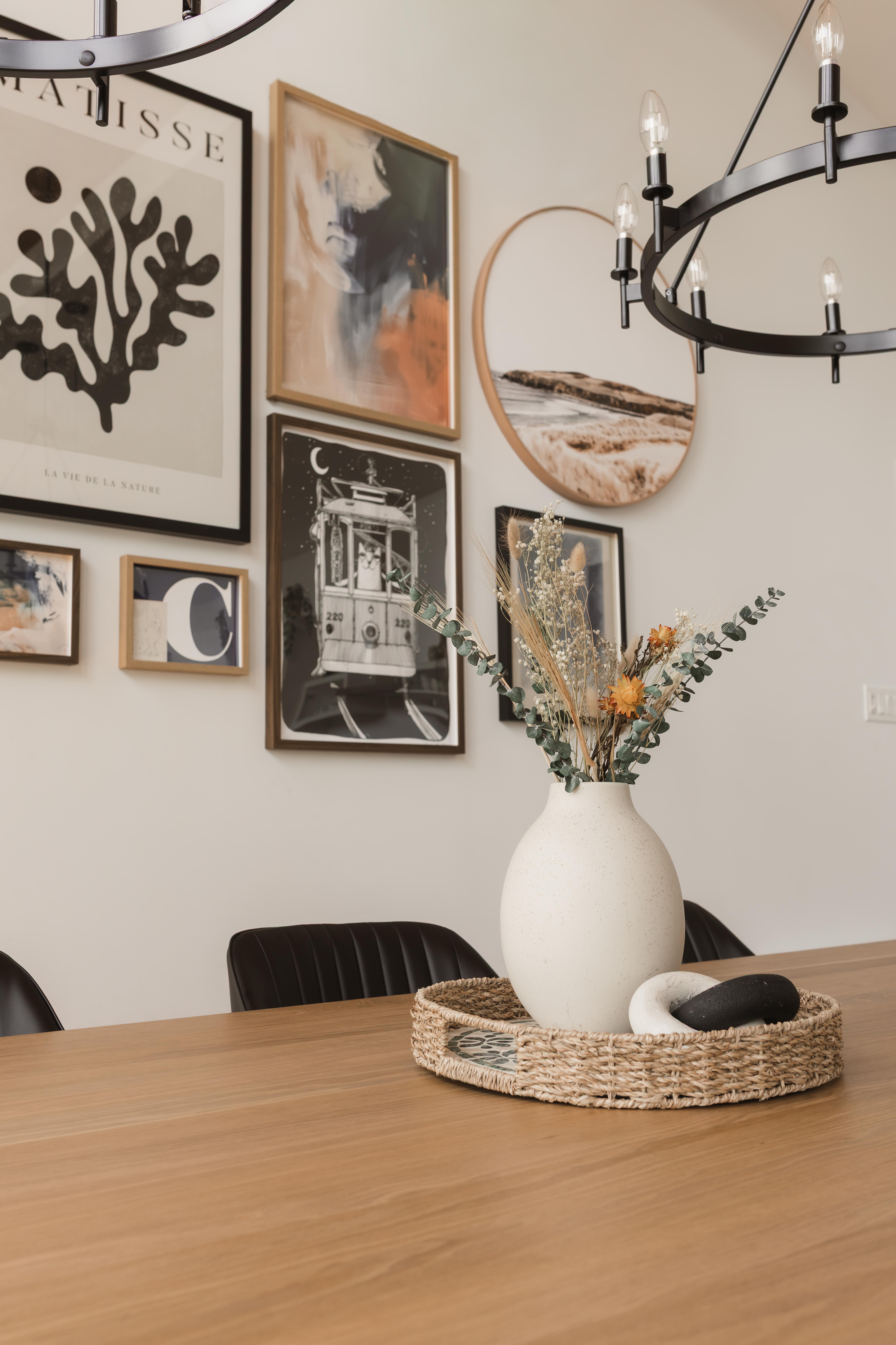 Mur de cadres (gallery wall), lustre noir et table à manger sur mesure en bois massif avec vase et plateau en osier | designer d'intérieur pour un chalet locatif à Beaulac-Garthby