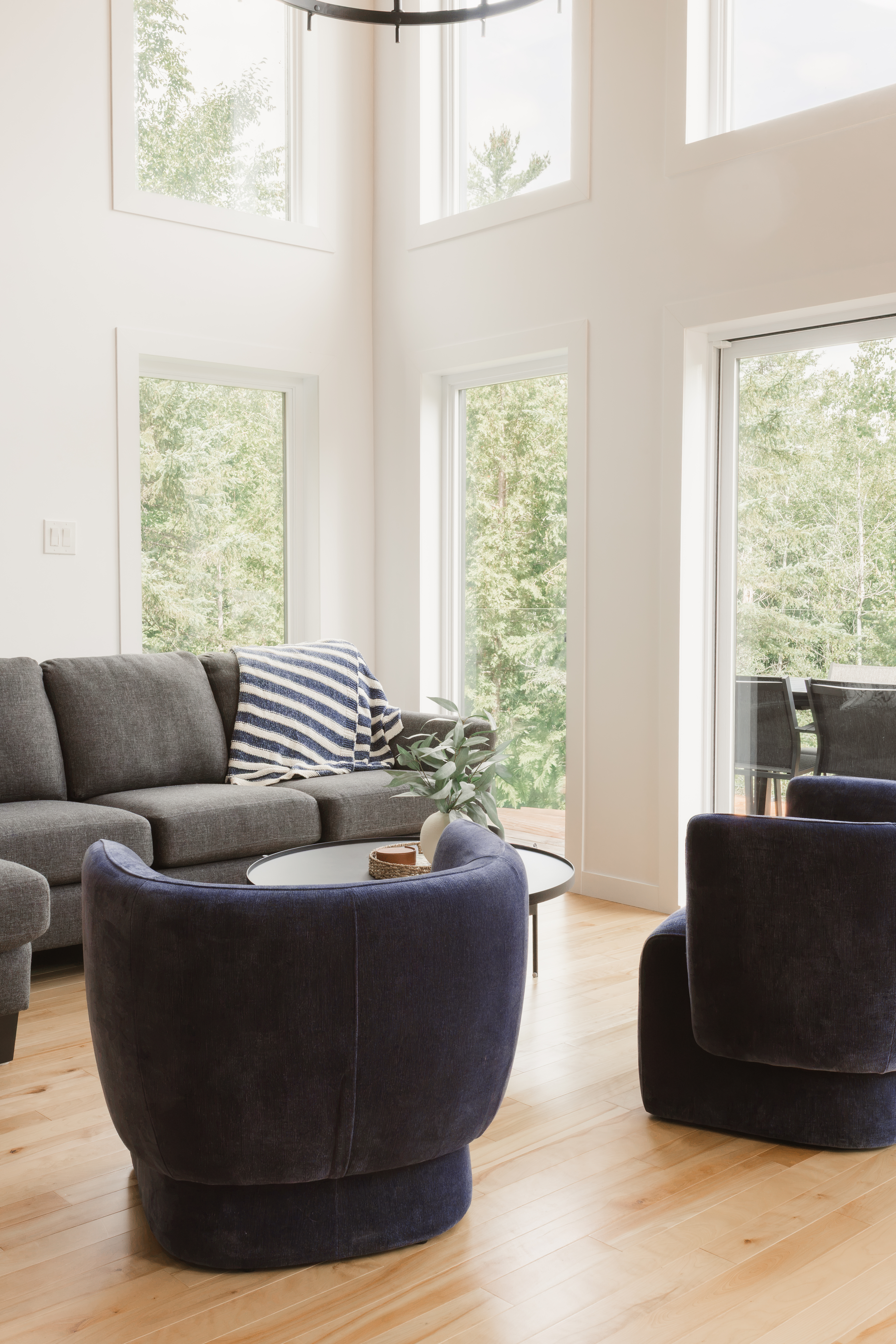 Salon à haut plafond en bois cathédrale avec fauteuils arrondis bleu marine, divan gris et grandes fenêtres | salon spacieux de chalet locatif | designer d'intérieur, Élévation Studio Design à Thetford Mines