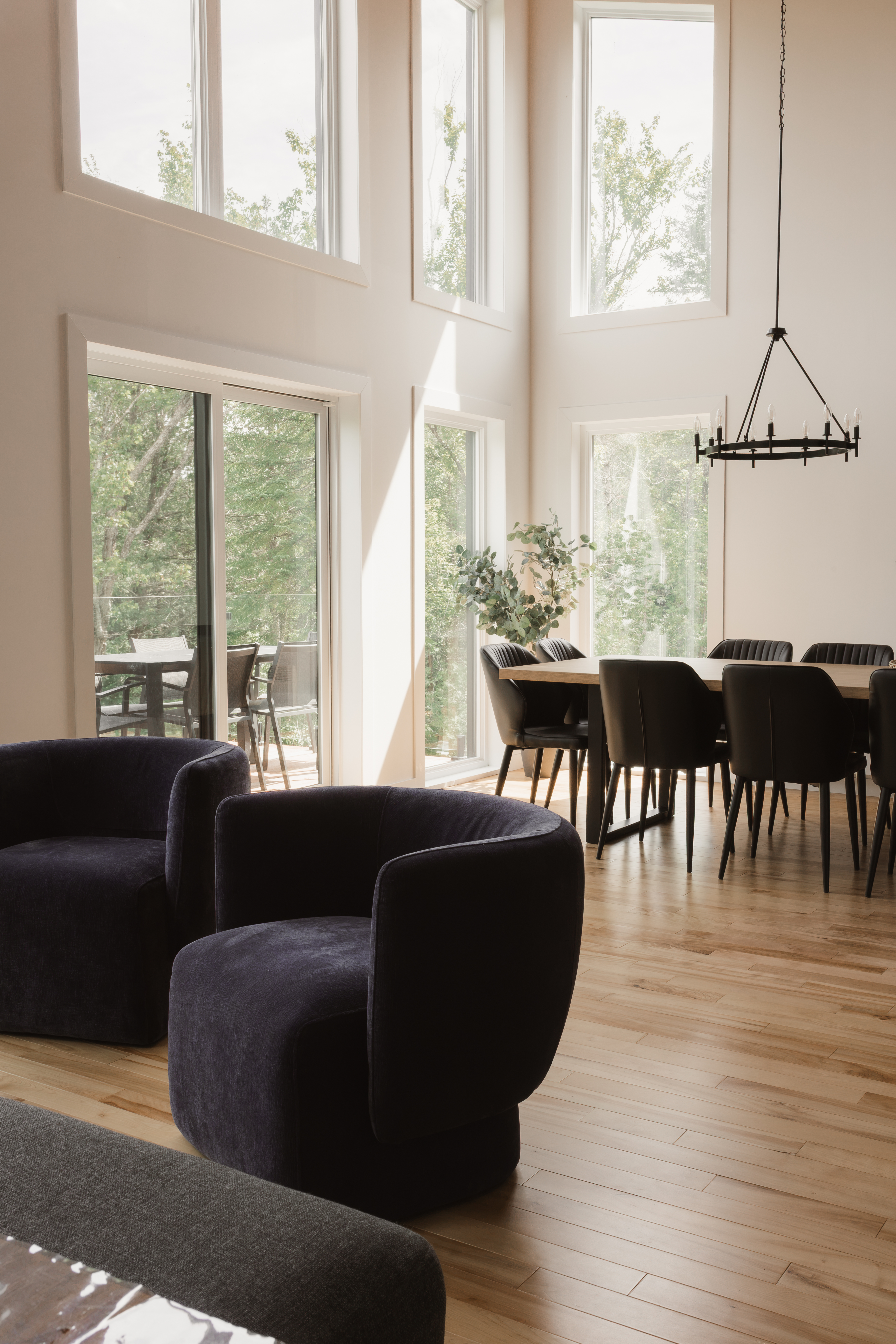 Fauteuils bleu marine devant la salle à manger, avec grandes fenêtres et lustre noir