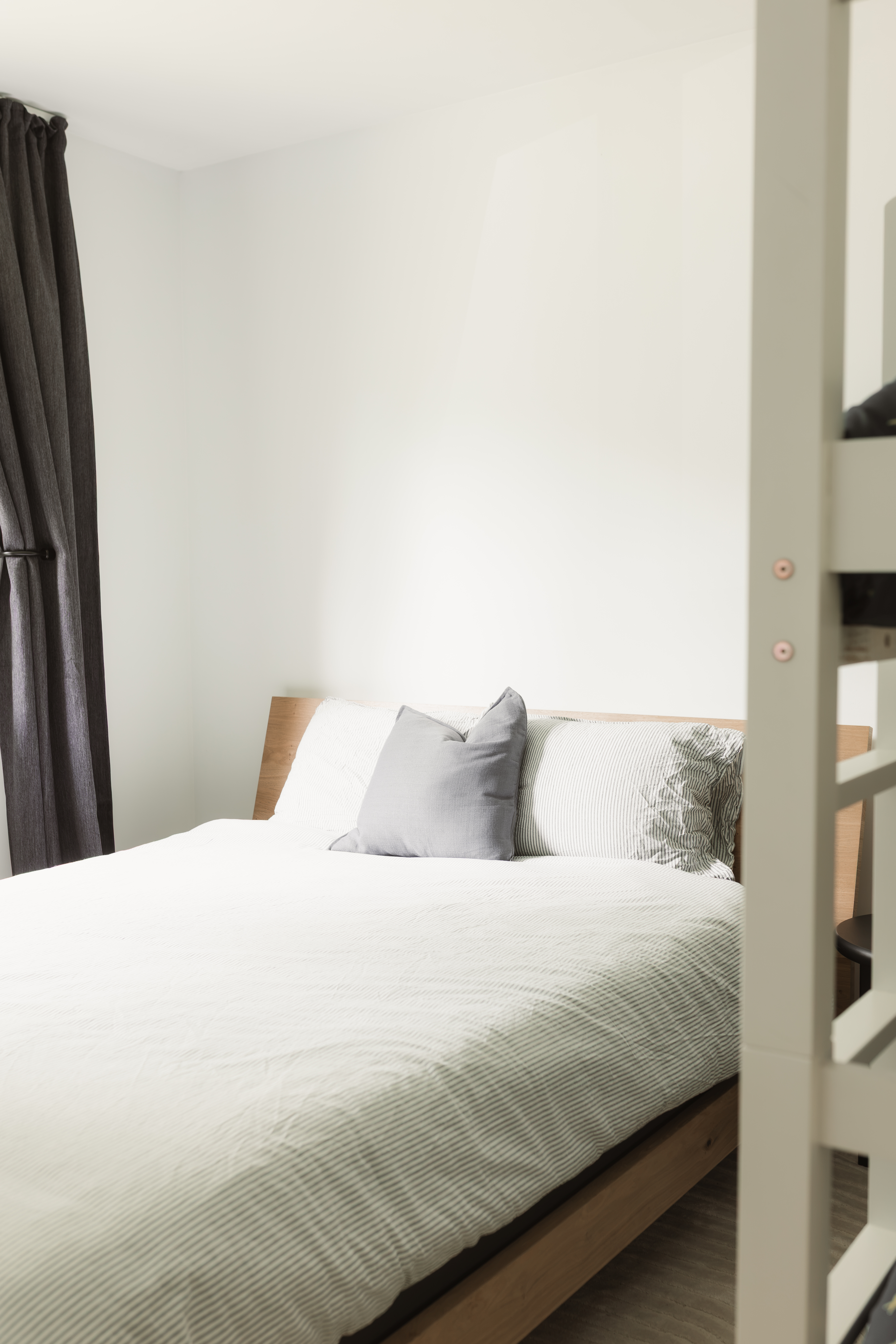 Une des quatre chambres : lit superposé et lit queen, literie blanche et coussins gris dans un chalet locatif à Beaulac-Garthby