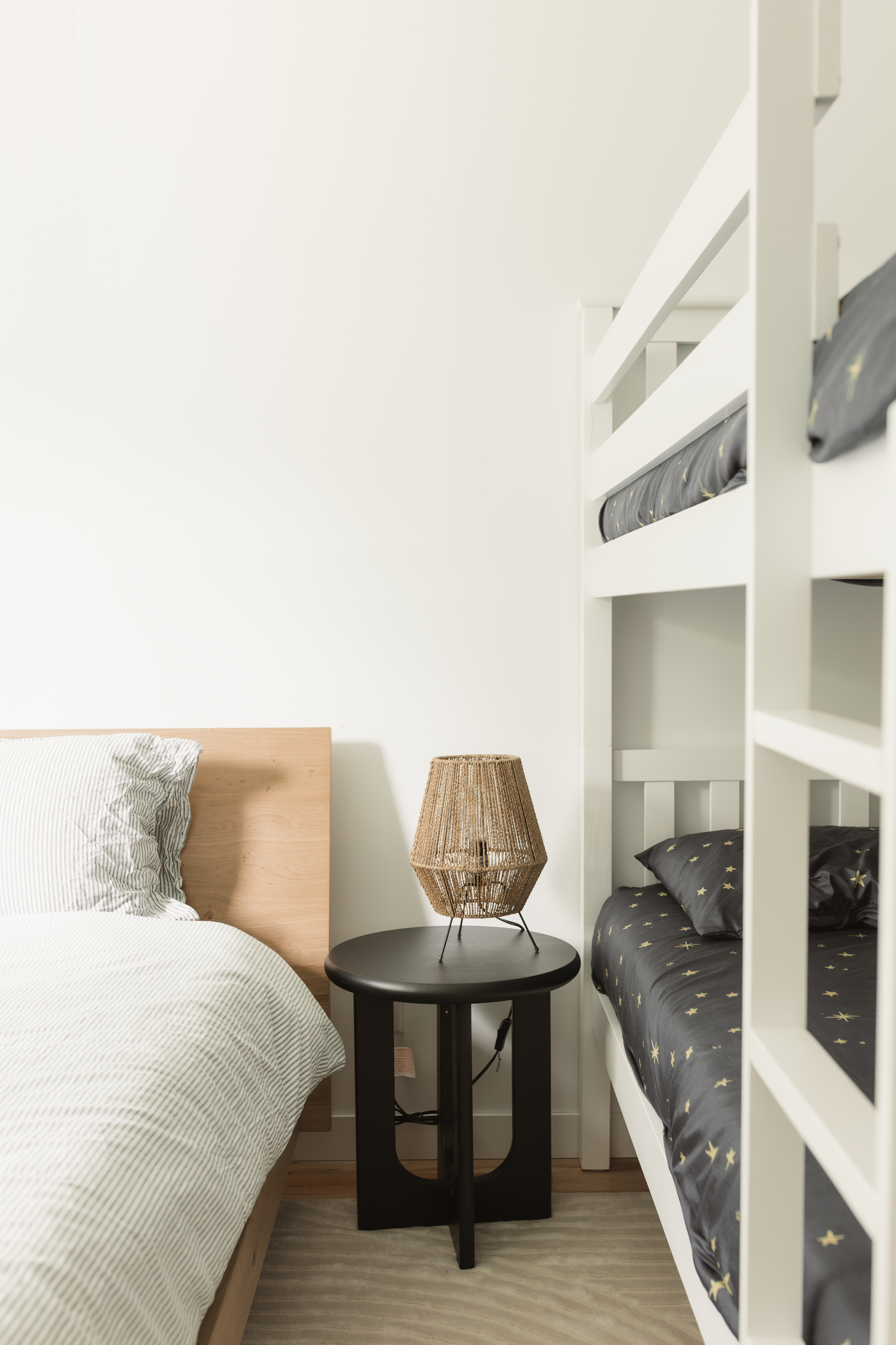 Une des quatre chambres du chalet locatif : lits superposés, lit queen et table de chevet ronde noire avec lampe d'ambiance